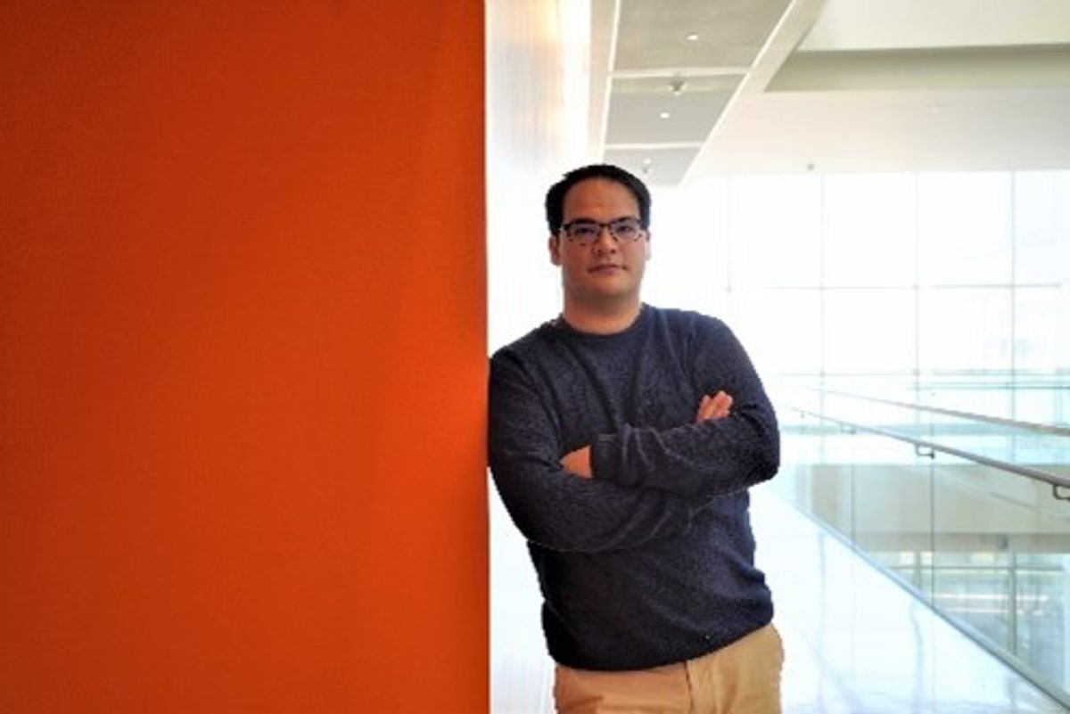 Pau Castel leans against a bright orange wall in a hallway.