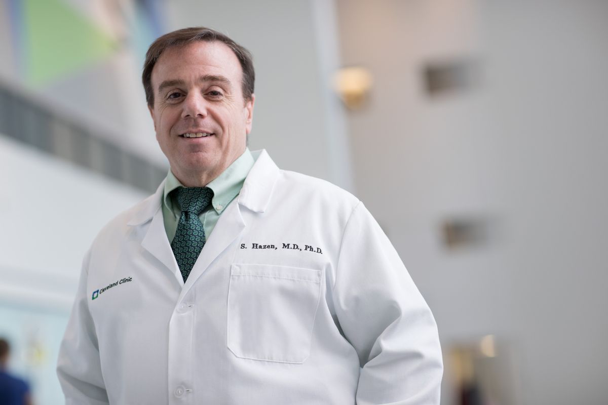 Stanley Hazen wears a white lab coat and stands in a lightly colored room.