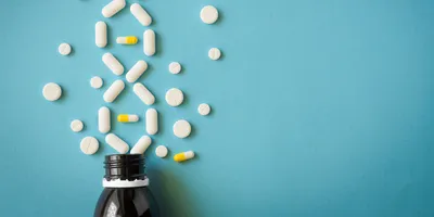 Pills scattered around a bottle arranged in the shape of a DNA strand, symbolizing the concept of pharmacogenomics. 