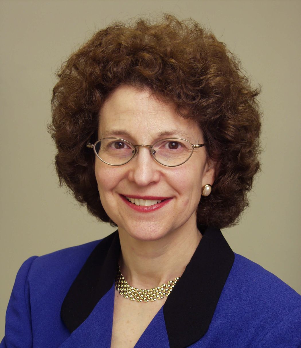 Amy Paller wears a blue dress and glasses in a headshot.