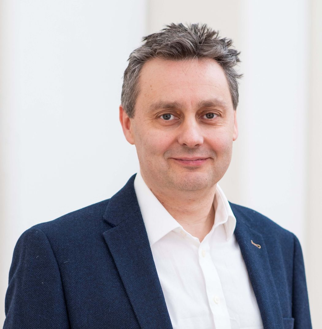 Stuart Cobb wears a blue suit jacket against a white background.