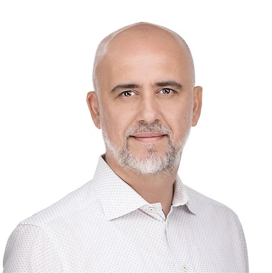 A headshot of Volkan Manga wearing a white shirt with purple dots. A headshot of Volkan Manga wearing a white shirt with purple dots.