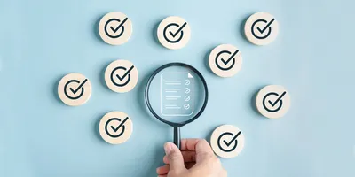 A magnifying glass highlights a checklist symbol surrounded by multiple checkmark icons, representing quality control, verification, and data integrity.