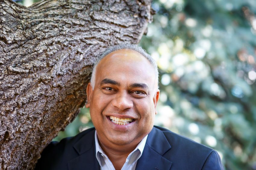 Gary Pestano, smiling in a suit standing outdoors beside a tree trunk. Gary Pestano, smiling in a suit standing outdoors beside a tree trunk.