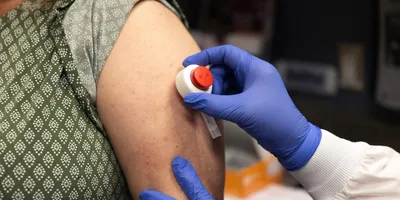 Healthcare worker wearing blue gloves using a microneedle device on a patient's arm for a blood draw. 