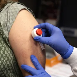 Healthcare worker wearing blue gloves using a microneedle device on a patient's arm for a blood draw. 