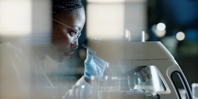 Black, female scientist using a microscope for analysis in a healthcare lab 