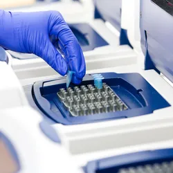 Image Alt Text	A laboratorian wearing blue gloves places a PCR sample into a real-time PCR thermocycler, the model shown is blue and white with a large digital screen.