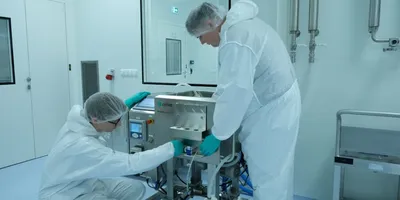 Two scientists in full cover interact with a machine in a lab