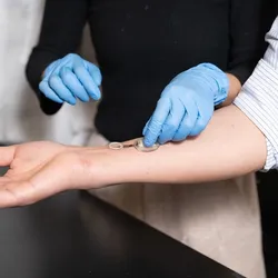 A person with gloves places a clear round device on the arm of another person.