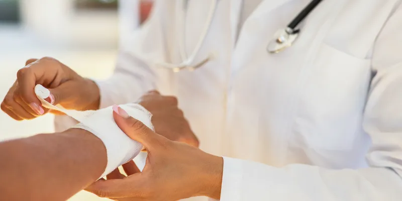 A female doctor in a lab coat wraps a bandage around a patients wrist
