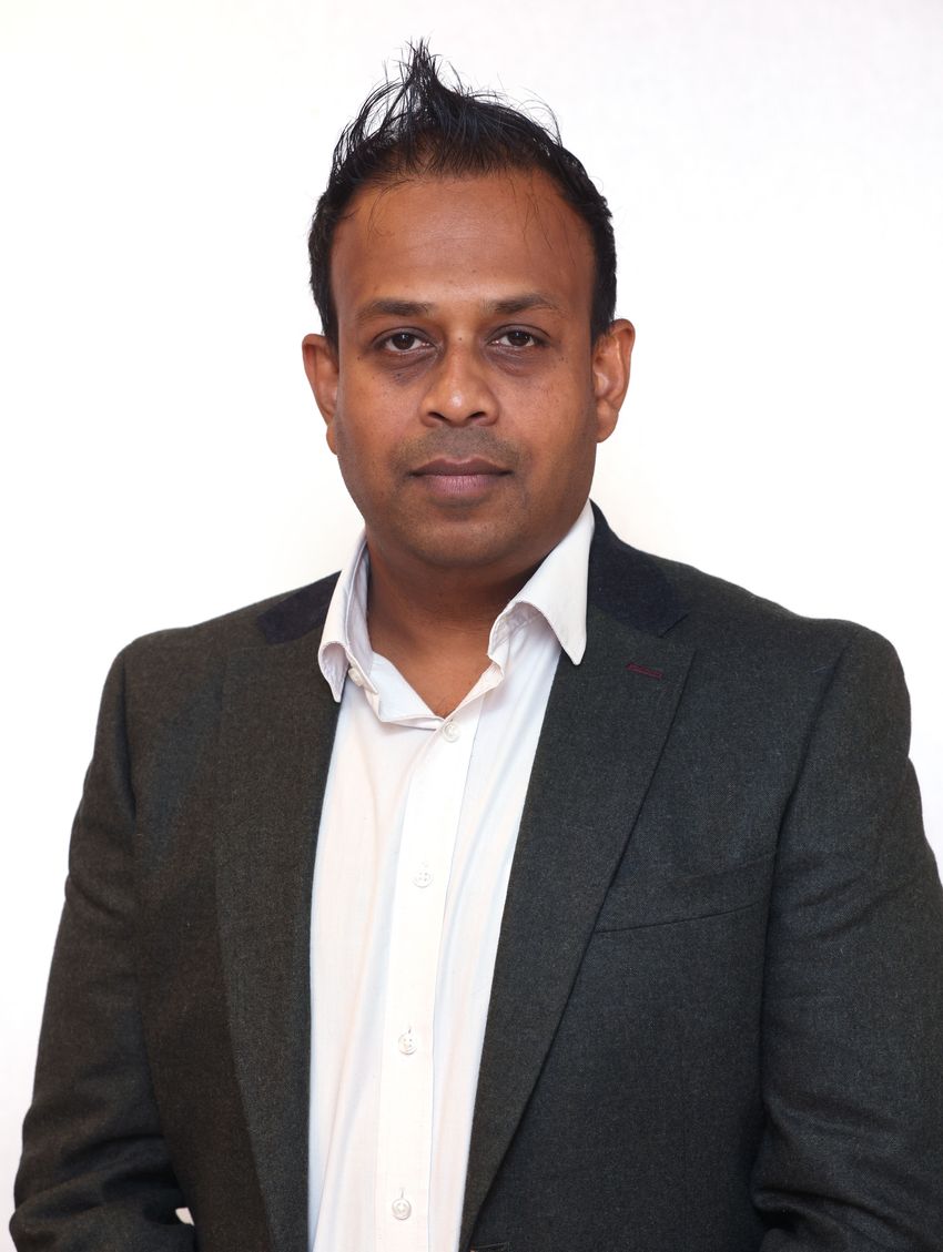 Muhunthan Thillai in a dark suit and white shirt posing against a plain white background. Muhunthan Thillai in a dark suit and white shirt posing against a plain white background.