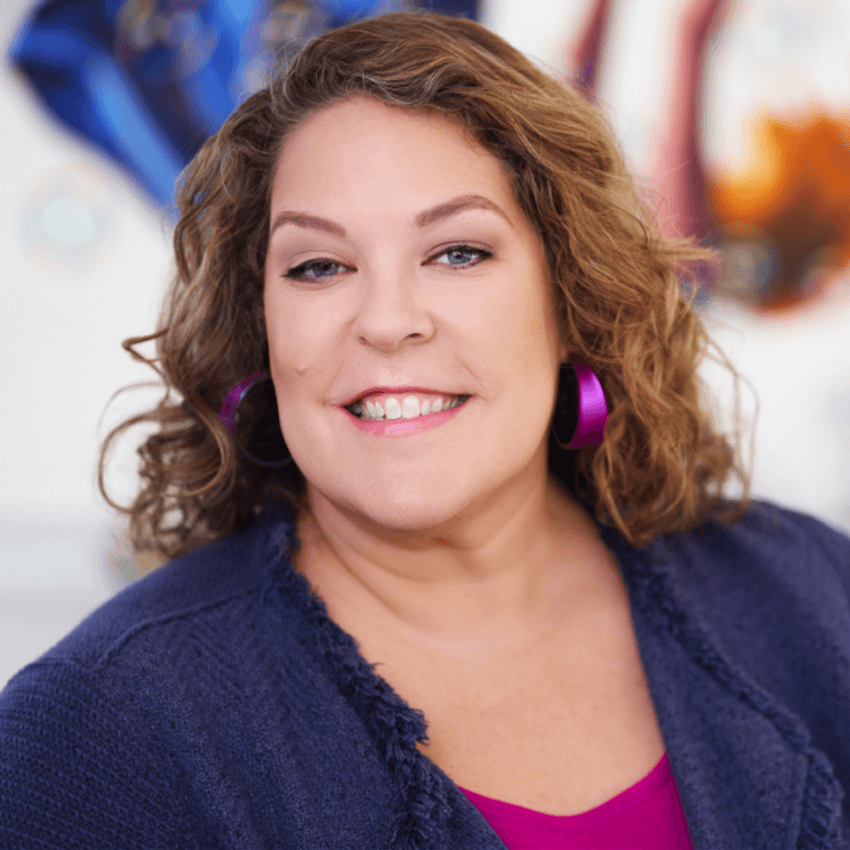 Lyn Baranowski smiling warmly in a purple top with curly hair and bold hoop earrings. Lyn Baranowski smiling warmly in a purple top with curly hair and bold hoop earrings.