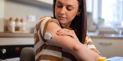 A woman looks at the glucose monitor on the back of her upper arm. 
