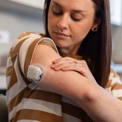 A woman looks at the glucose monitor on the back of her upper arm. 
