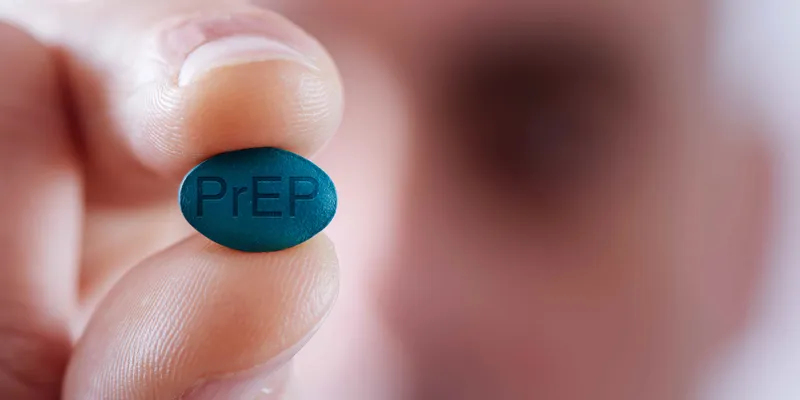 A blurred-out man in the background holds a blue pill that says PrEP in the foreground.