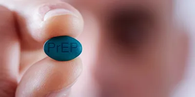 A blurred-out man in the background holds a blue pill that says PrEP in the foreground.