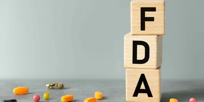 Block letters spell out FDA with pills on the ground next to them.