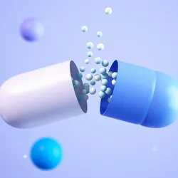 A 3D illustration of a capsule splitting open to release small white and blue granules, surrounded by floating pills and spheres on a light blue background.