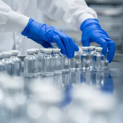 Gloved hands working in pharmaceutical factory manufacturing sterile bottles