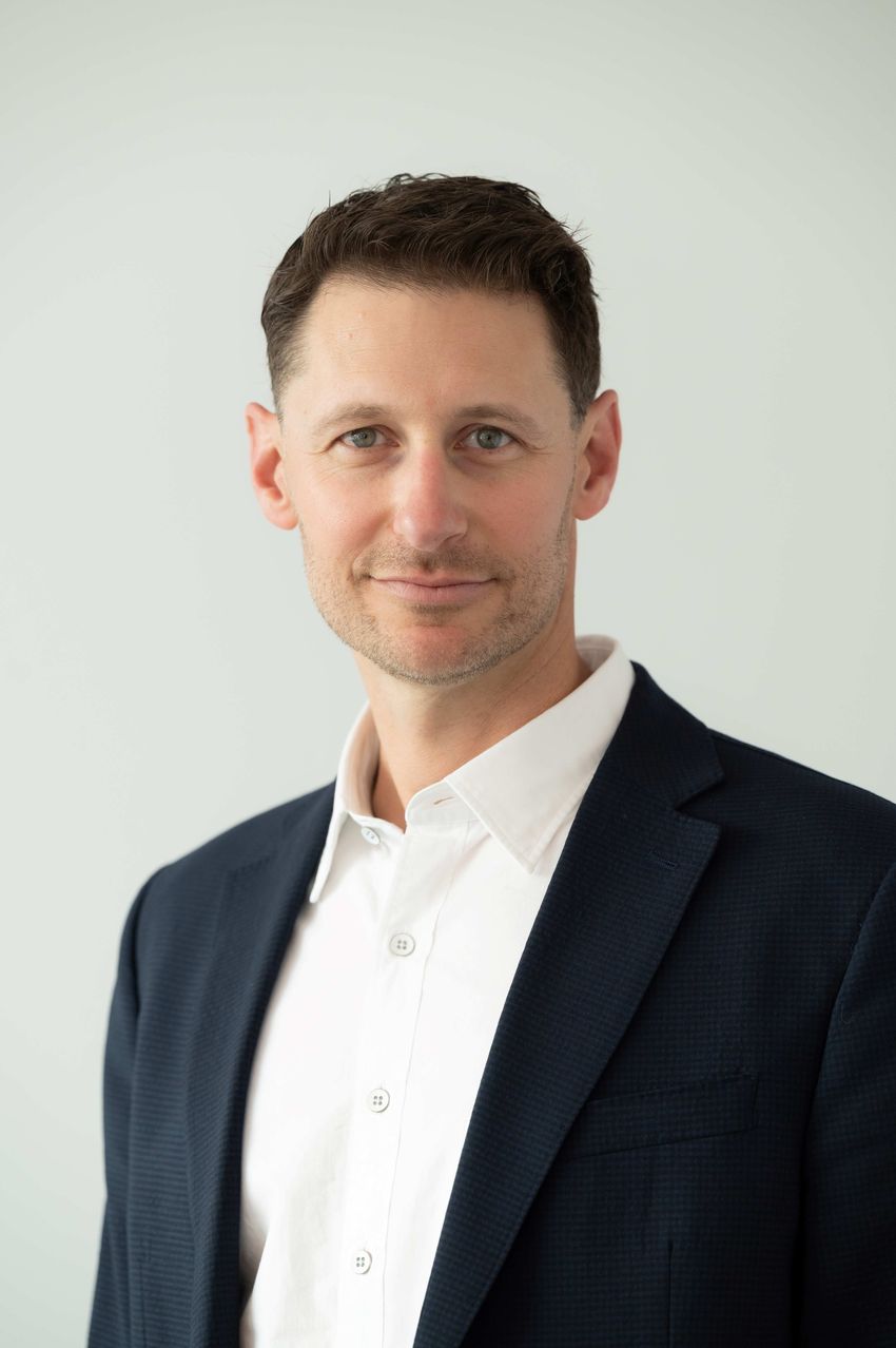 Brian Safina wears a white button down shirt and navy suit on a gray background.