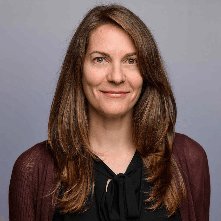 Erica Frew smiling in a professional headshot, wearing a black blouse and maroon cardigan against a gray background.