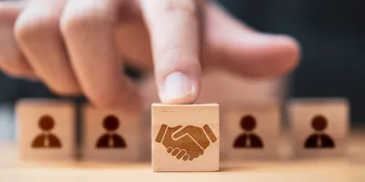 Hand placing a wooden cube block with a picture of hands shaking in front of human icons for business deal and agreement concept.