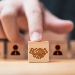 Hand placing a wooden cube block with a picture of hands shaking in front of human icons for business deal and agreement concept.