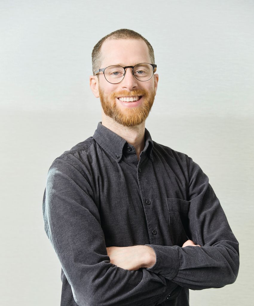 Benedict Cross, smiling with glasses and a beard wearing a dark shirt, standing confidently with arms crossed. Benedict Cross, smiling with glasses and a beard wearing a dark shirt, standing confidently with arms crossed.