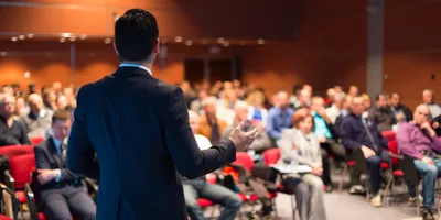 A male speaker presenting to an audience at a scientific conference.