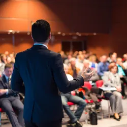 A male speaker presenting to an audience at a scientific conference.