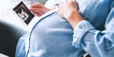 Woman laying hand on her pregnant belly while looking at picture of baby 