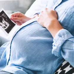 Woman laying hand on her pregnant belly while looking at picture of baby 