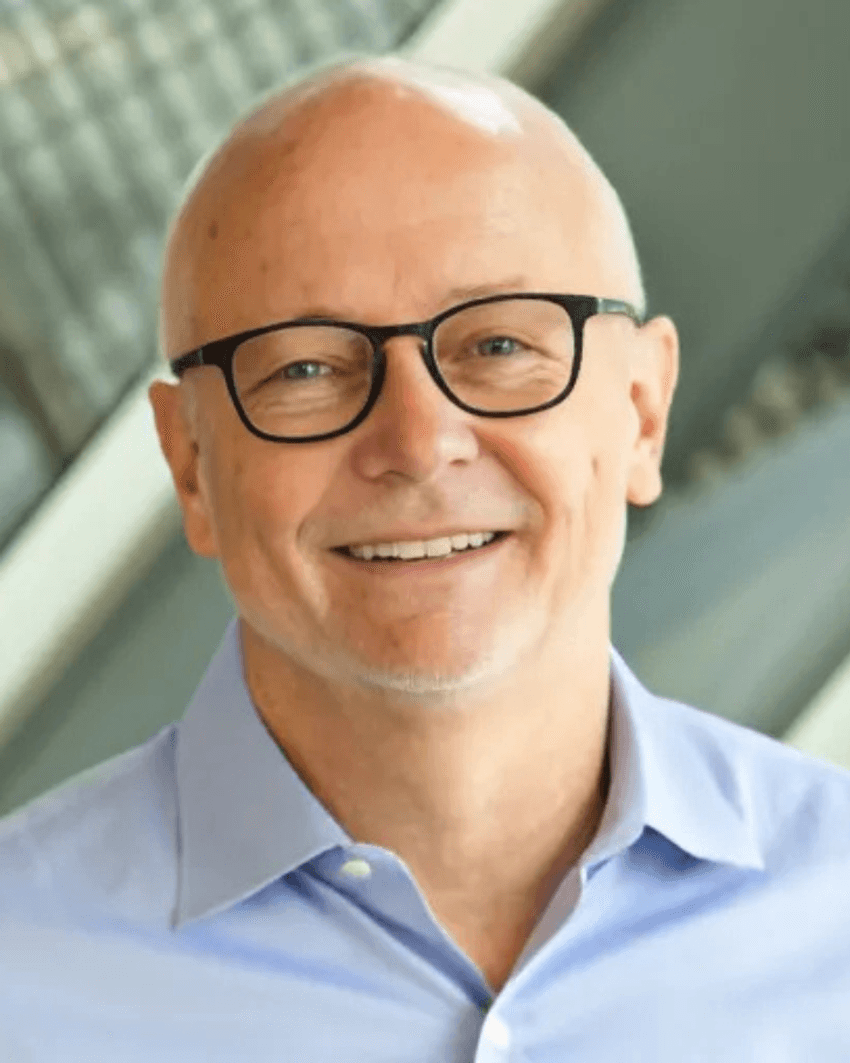 Phil Johnson smiles wearing black glasses and a light blue shirt.