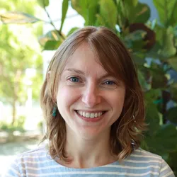 Yelena, smiling outside in front of foliage 