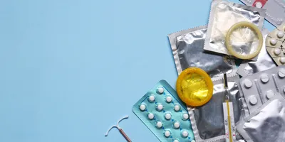 Different birth control methods including contraceptive pills, condoms, intrauterine device, and thermometer on a light blue background.