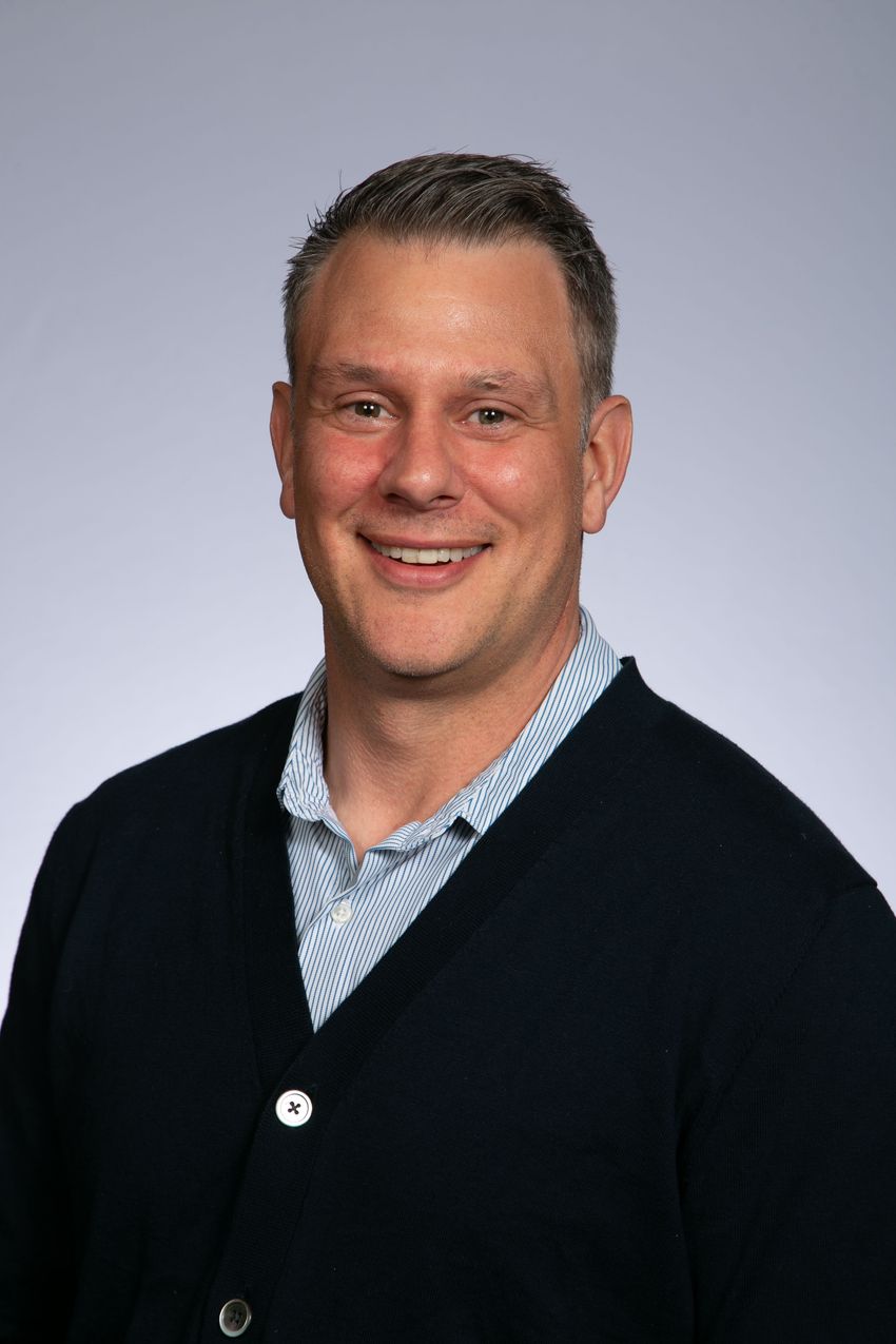 Scott Baver smiling in front of plain background.