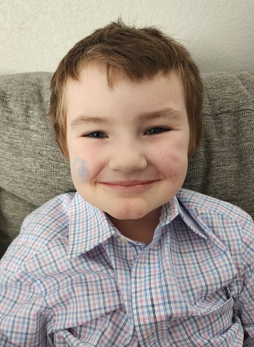 A boy in a checkered black, blue, and red shirt smiling and sitting on a sofa. A boy in a checkered black, blue, and red shirt smiling and sitting on a sofa.