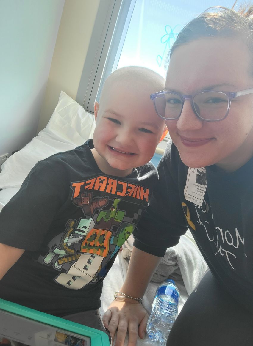 A boy in a black T-shirt sitting on a hospital bed next to his mother who is also wearing a black shirt. A boy in a black T-shirt sitting on a hospital bed next to his mother who is also wearing a black shirt.