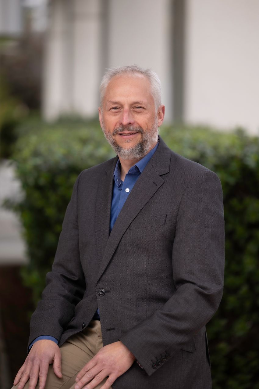 Sean Tucker wears a gray suit and dark blue button-down shirt and sits outside.