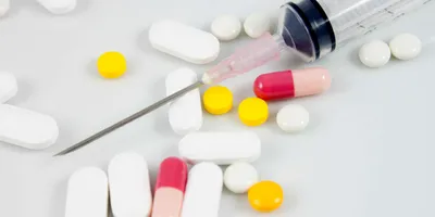A variety of oral pills are shown on a white background with a syringe needle on top.