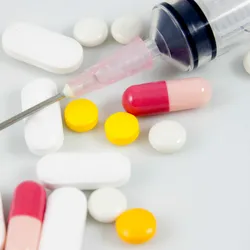 A variety of oral pills are shown on a white background with a syringe needle on top.