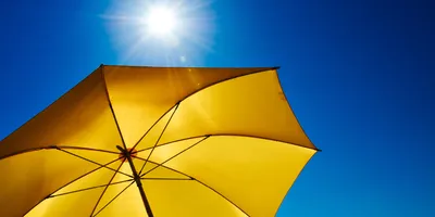 A bright yellow umbrella is shown under the sun and a blue sky.