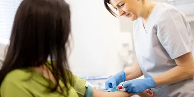 Senior nurse takes a venous blood test from the arm of a young woman in laboratory for breast cancer screening.
