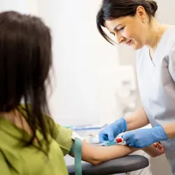 Senior nurse takes a venous blood test from the arm of a young woman in laboratory for breast cancer screening.