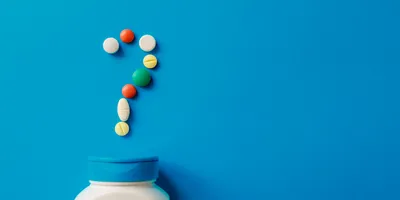 Pills spilling out of a tub, forming a question mark, on a blue background.