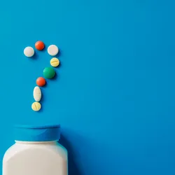 Pills spilling out of a tub, forming a question mark, on a blue background.