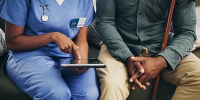 Female nurse talks to clinical trial patient, using a tablet. 
