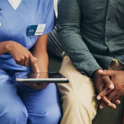 Female nurse talks to clinical trial patient, using a tablet.