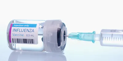 A clear bottle that says influenza vaccine with a syringe.